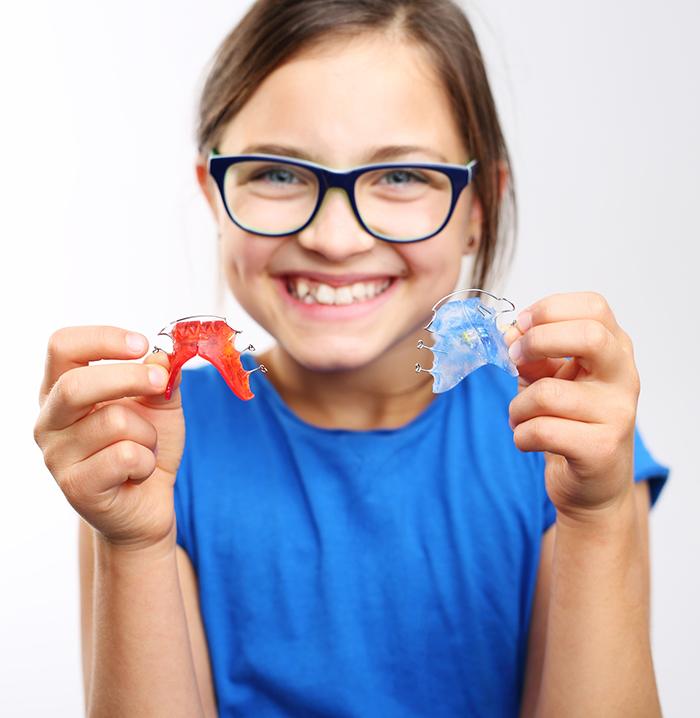 Young girl holding a red and blue dentofacial orthopedics appliances