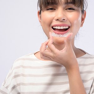 Woman with bangs smiling while putting on Invisalign