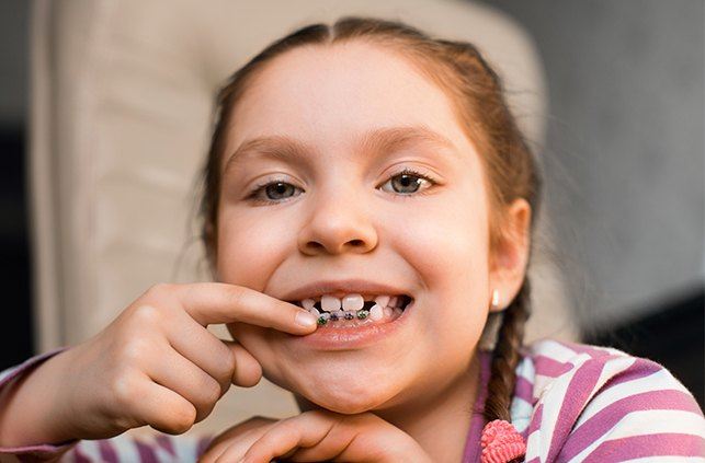 Young girl pointing to her pediatric orthodontic appliance