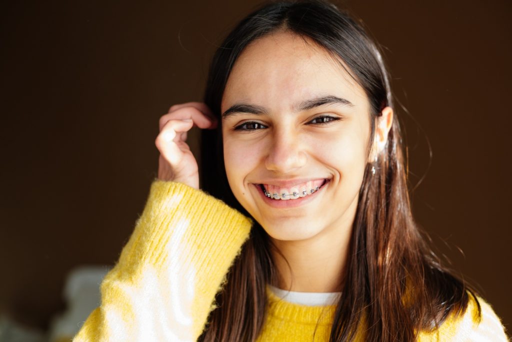 Girl with braces smiling while tucking hair behind her ear