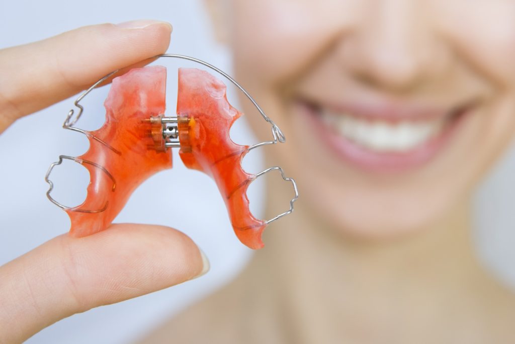 Woman smiling while holding up orthodontic retainer