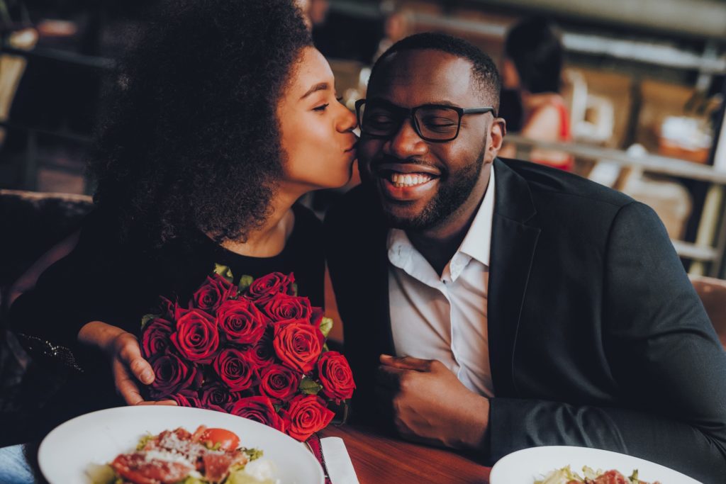 Girl with red roses kissing date on the cheek