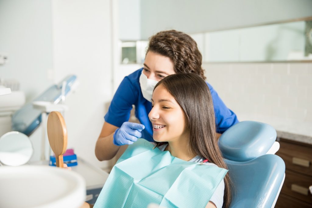 Orthodontist smiling while patient looks at braces in mirror